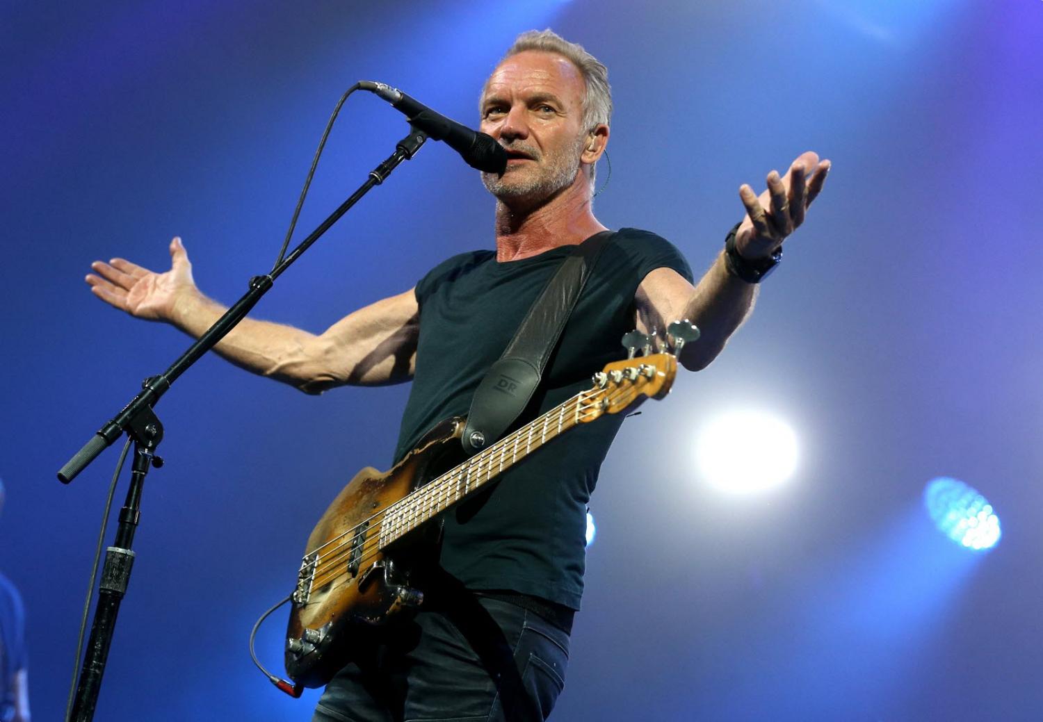 Sting, bras ouverts, sur scène, parlant ou chantant dans un microphone.